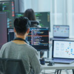 Asian software developers working on multiple screens displaying code and application diagrams in a modern office