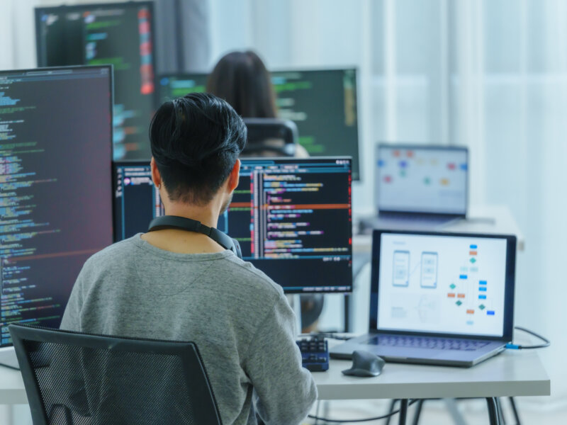 Asian software developers working on multiple screens displaying code and application diagrams in a modern office